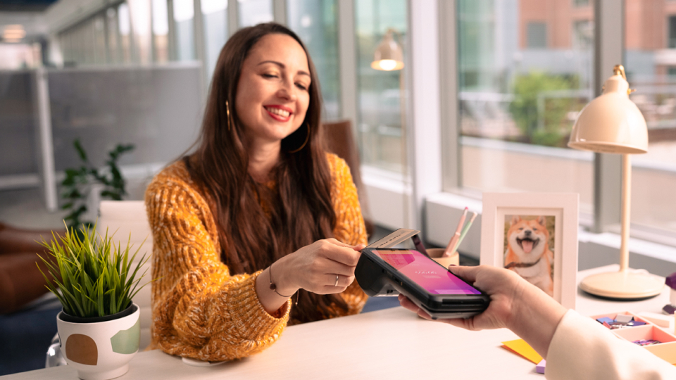 Merchant holding a credit card machine to a customer paying with her phone